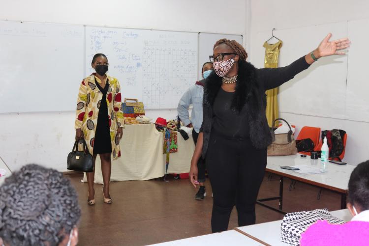 Ms. Connie a fashion design lecturer gestures at the students while a model poses in an outfit