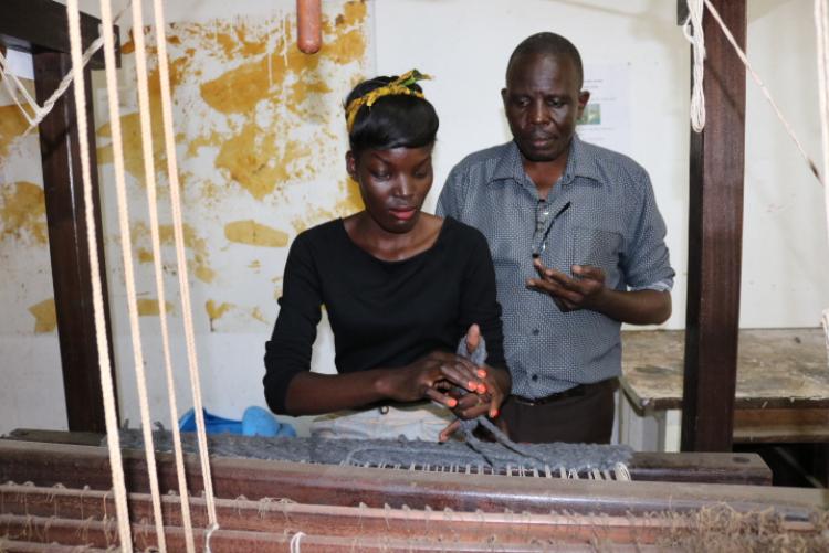 A student learning and being guided on  how to thread a loom machine 